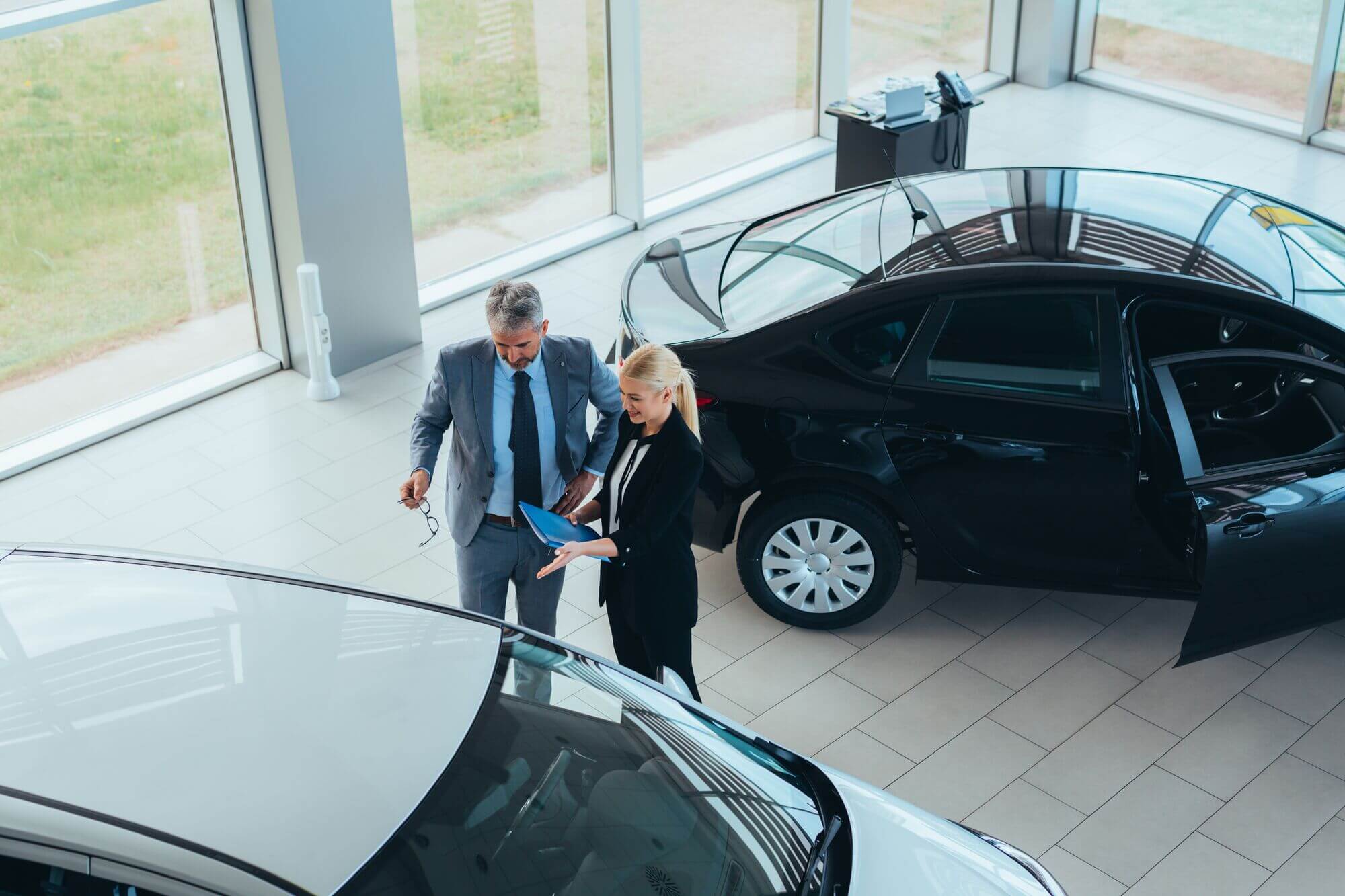 Overhead view of car dealer and customer reviewing used electric vehicle on dealership showroom floor