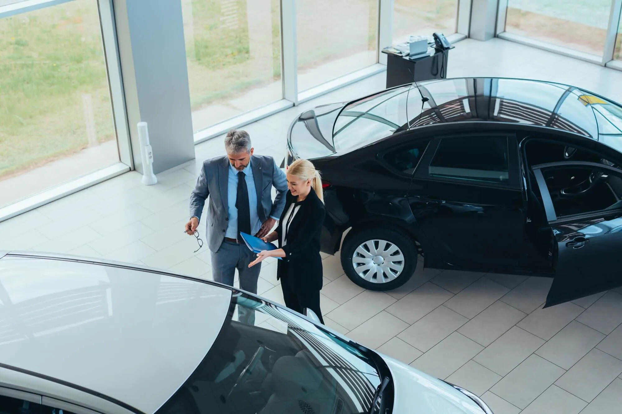 Overhead view of car dealer and customer reviewing used electric vehicle on dealership showroom floor